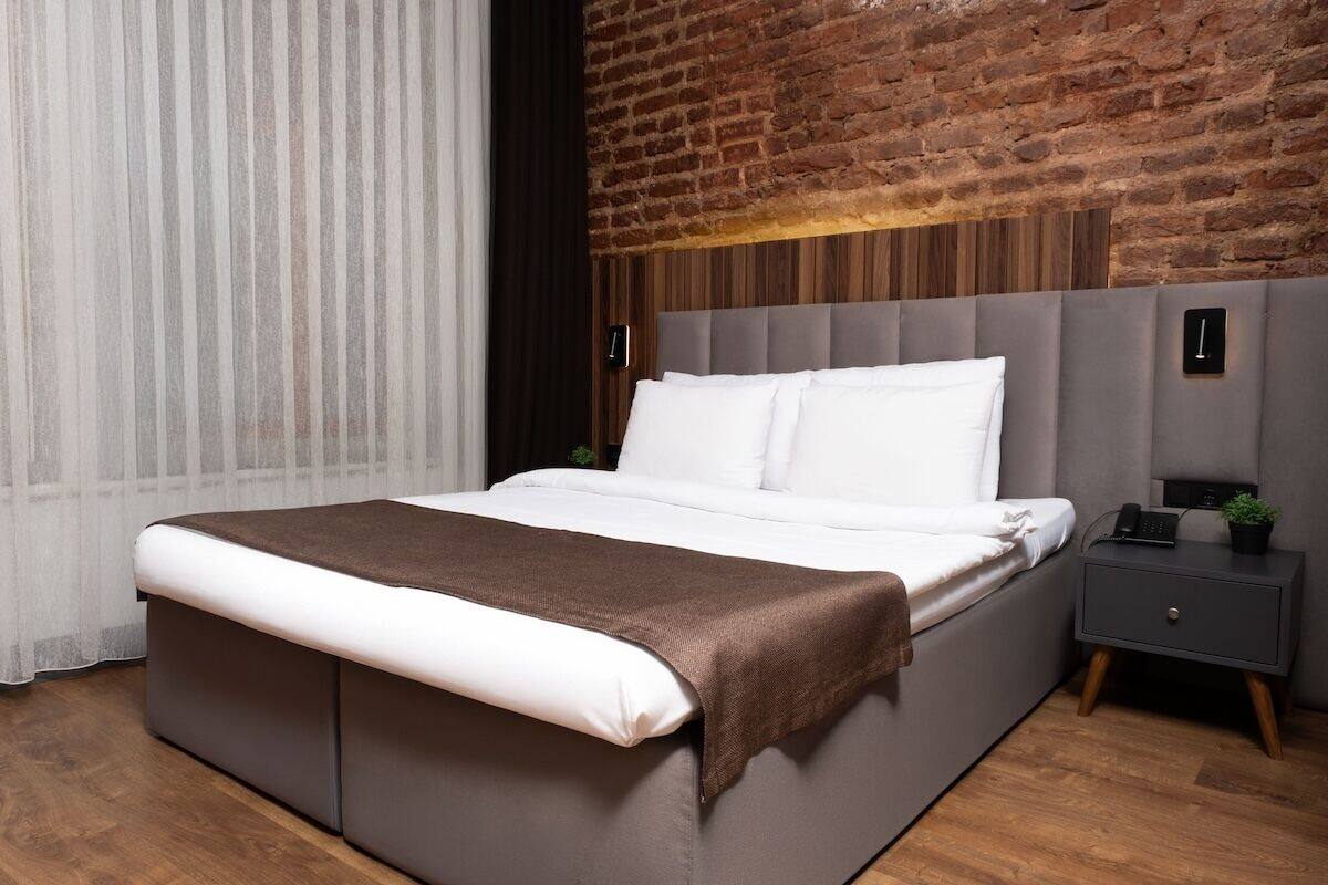 A modern bedroom with a large bed, a nightstand, and a brick wall.