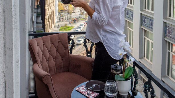 Ein Balkon mit Blick auf die Stadt, ein Tisch mit einem Stuhl und eine Person, die ein Tablett hält.