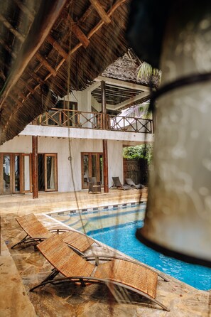 A pool area with lounge chairs and a thatched roof structure. - Tamani Villas (Matemwe)