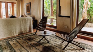 A room with a bed, two chairs, a patterned rug, and large windows with a view of greenery. - Tamani Villas (Matemwe)