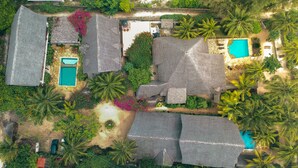 An aerial view of a resort with multiple buildings, including a pool area, surrounded by lush greenery and palm trees. - Tamani Villas (Matemwe)