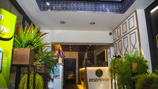 A hotel reception area with a modern design, including a reception desk, plants, and a skylight. - Can Grand Hotel  (Ankara)