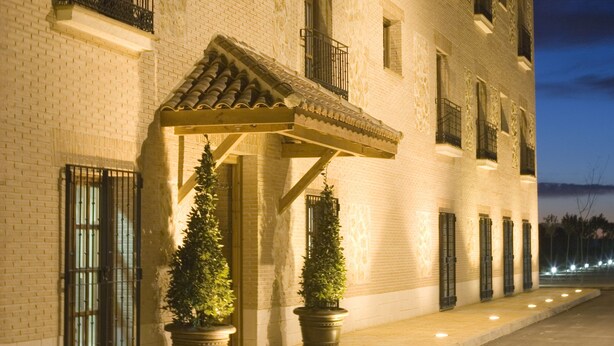 Un edificio de varios pisos con fachada de ladrillo, un acceso cubierto y plantas en macetas.