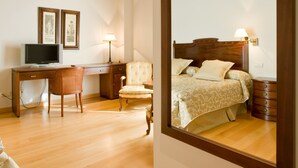 Una habitación de hotel con techo de madera, una cama grande con cabecera de madera, un escritorio con computadora, una silla y una mesita de noche con lámpara.