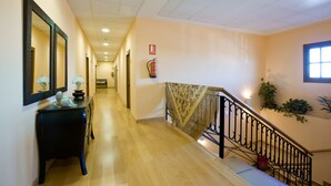 Un pasillo de hotel con piso de madera, una consola negra con lámpara, un espejo y un extintor.