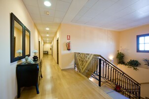 A hotel hallway with a wooden floor, a black console table with a lamp, a mirror, and a fire extinguisher.