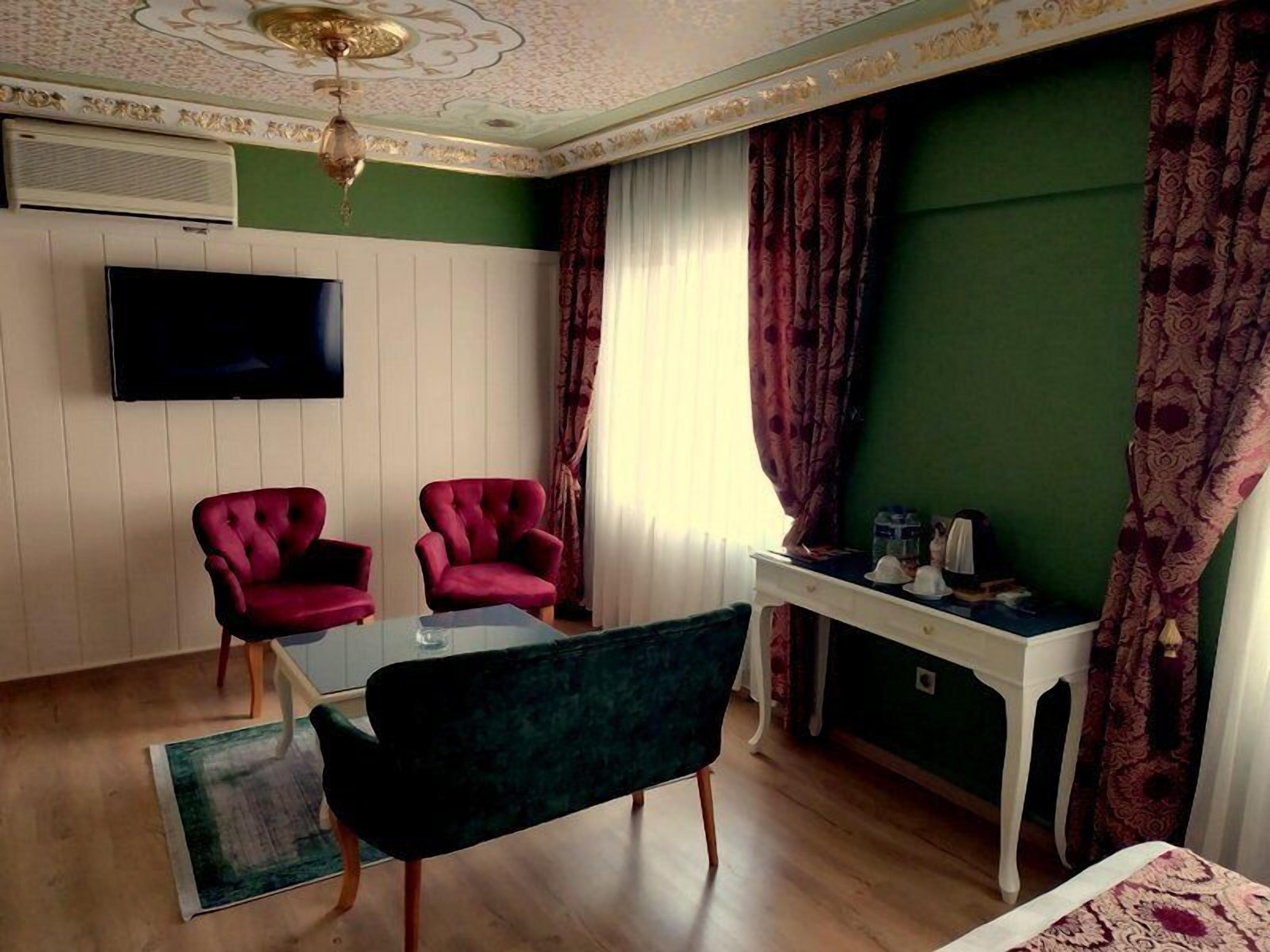 A room with two red armchairs, a glass table, a green sofa, a white desk, and a television on the wall.