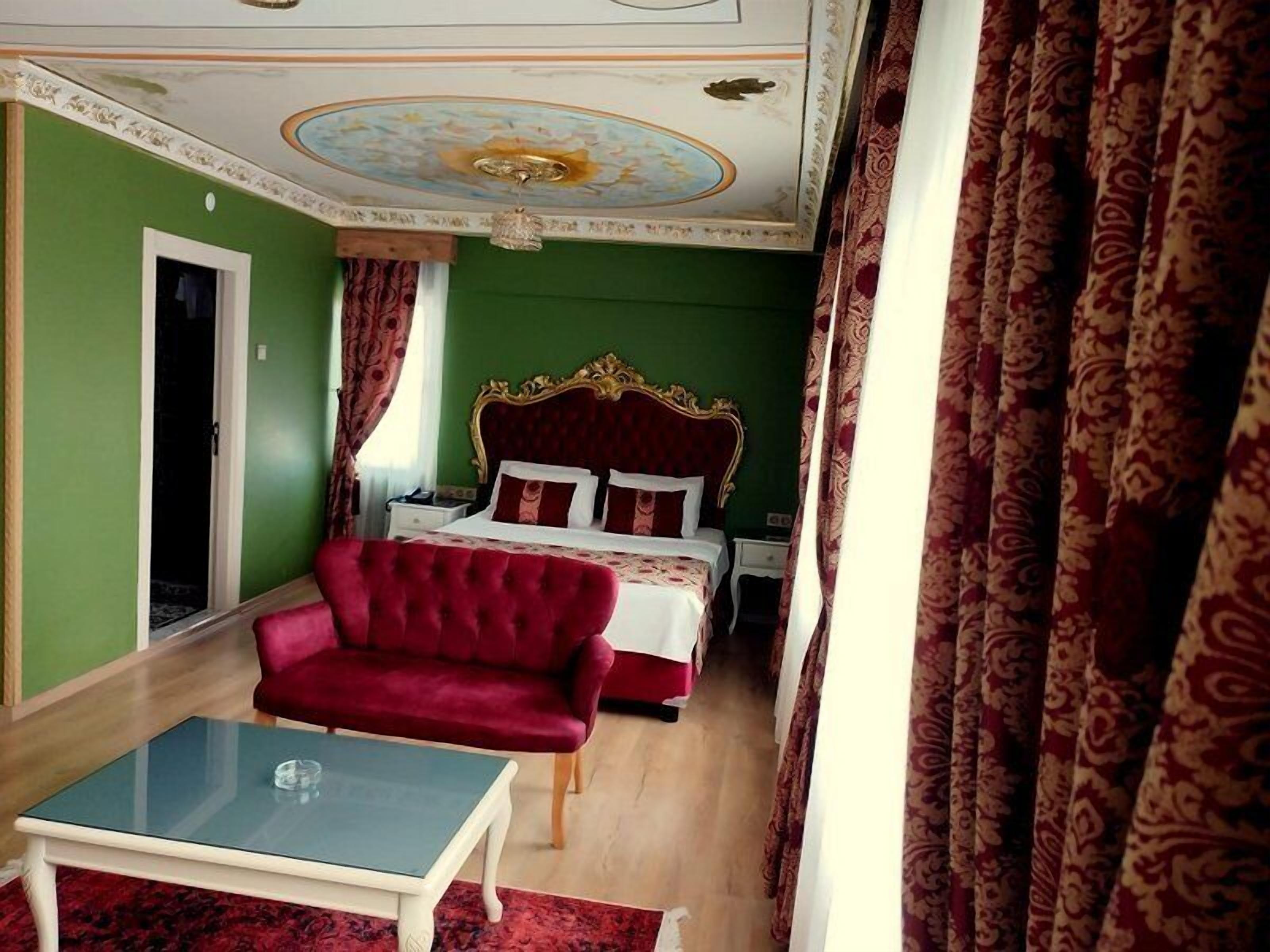 A hotel room with a large bed, a red armchair, a glass-top table, and a green wall.