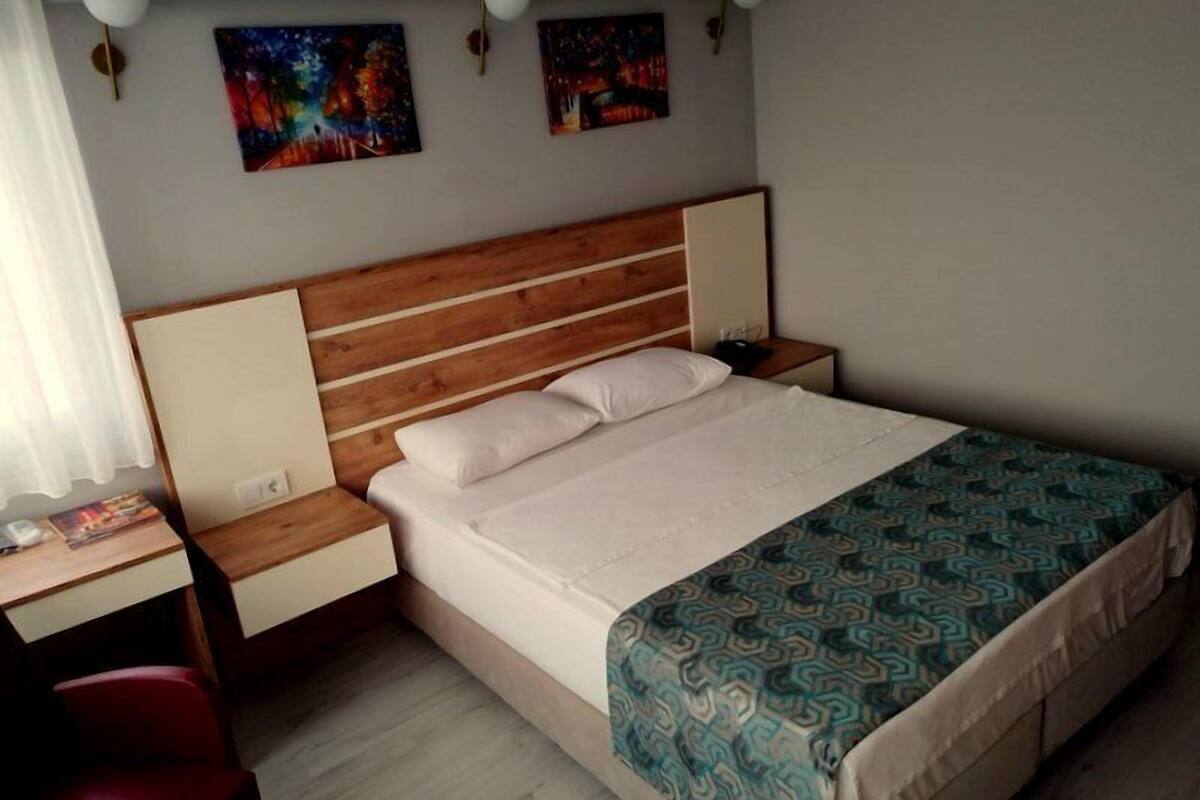 A neatly arranged bedroom with a wooden headboard, a bed with white linens, a patterned bedspread, and two wall-mounted lamps.