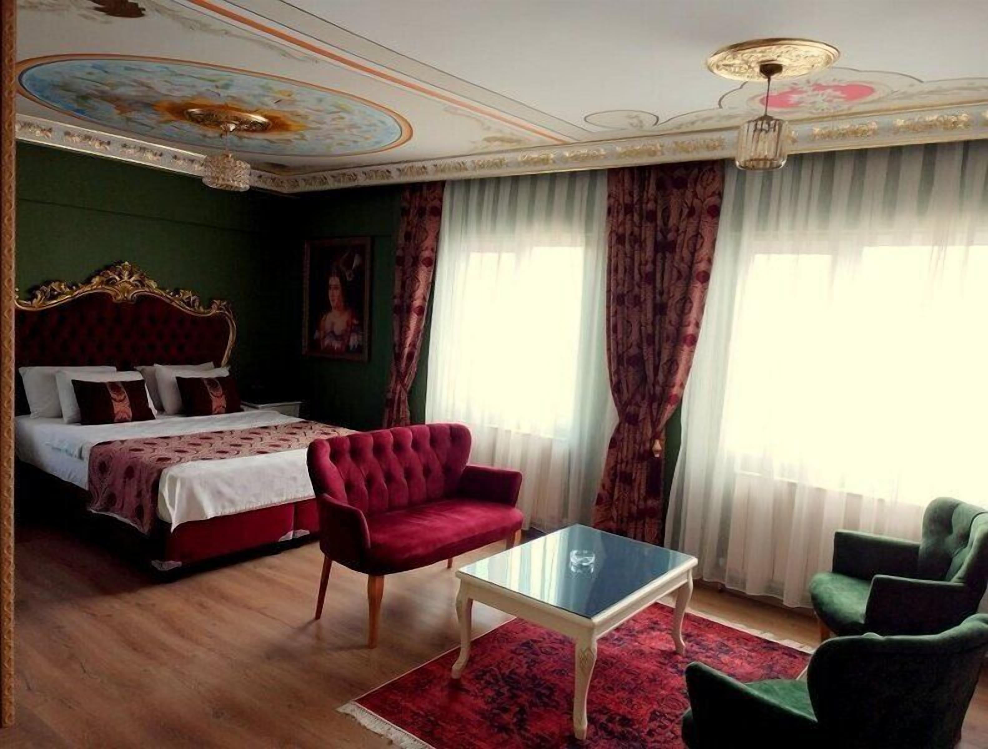 A hotel room with a large bed, a red armchair, a glass coffee table, and a green armchair.
