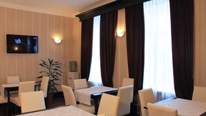 Un espace repas d’hôtel avec des tables et des chaises, un téléviseur fixé au mur et une plante en pot.