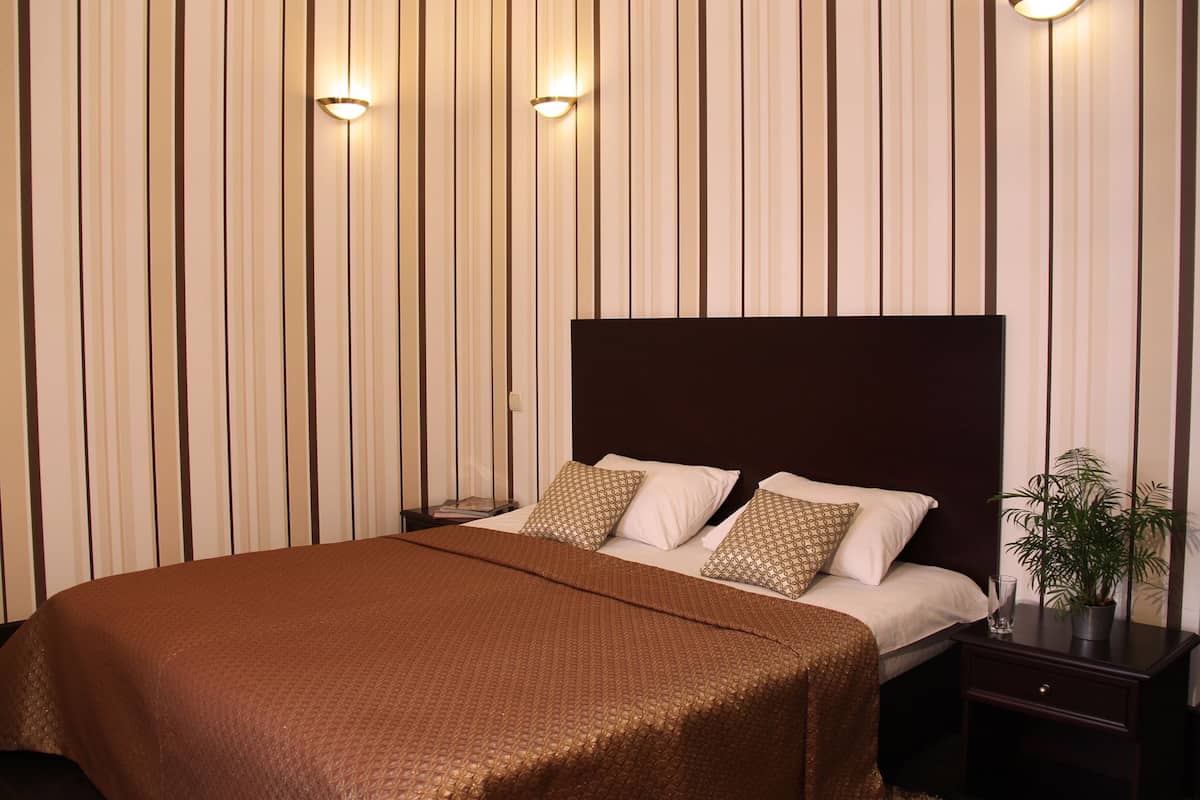 A hotel room with a large bed, two bedside tables, a nightstand, and a potted plant.