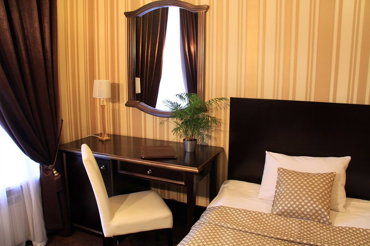 A hotel room with a bed, a desk, a chair, a lamp, and a potted plant.