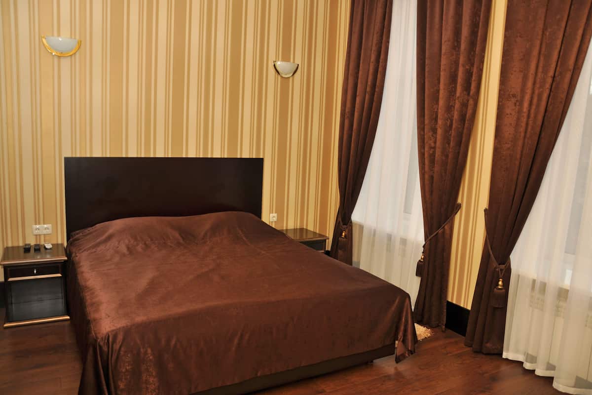 A hotel room with a large bed, a nightstand, a lamp, and curtains.