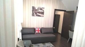 Un salon comprenant un canapé, une petite table, un fauteuil, un tapis à motifs et un mur orné d’un tableau.