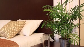 Un lit bien fait, agrémenté d’oreillers à motifs, un vase en verre transparent et une plante en pot posés sur une table de chevet en bois.