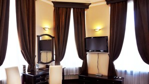 Une chambre d’hôtel dotée d’une grande fenêtre, de rideaux occultants, d’un téléviseur à écran plat, d’un miroir, d’un bureau et de deux chaises.