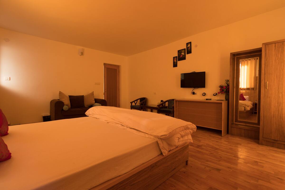 A bedroom with a bed, wooden wardrobe, desk, chair, and a television on the wall.