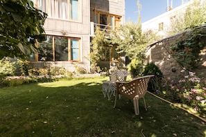 A modern building with large windows, a well-maintained garden with a lawn and patio furniture, and a stone wall with climbing plants. - Radhu's Boutique Inn (Leh)