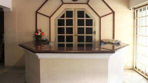 A reception desk with a clock above it, a flower vase, and a telephone on the counter. - Hotel Keerthi (Thiruvananthapuram)