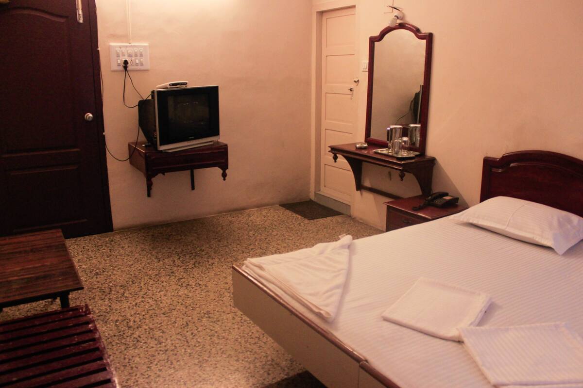 A hotel room with a bed, a bedside table, a television, a mirror, and a door.