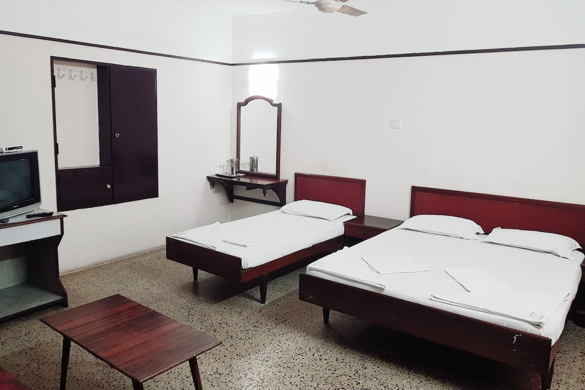 A hotel room with two single beds, a desk with a television, a mirror, and a ceiling fan.
