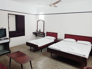 A hotel room with two single beds, a desk with a television, a mirror, and a ceiling fan.
