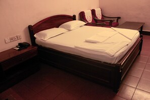 A single bed with a wooden headboard, a bedside table with a phone, and a chair with a red cushion.
