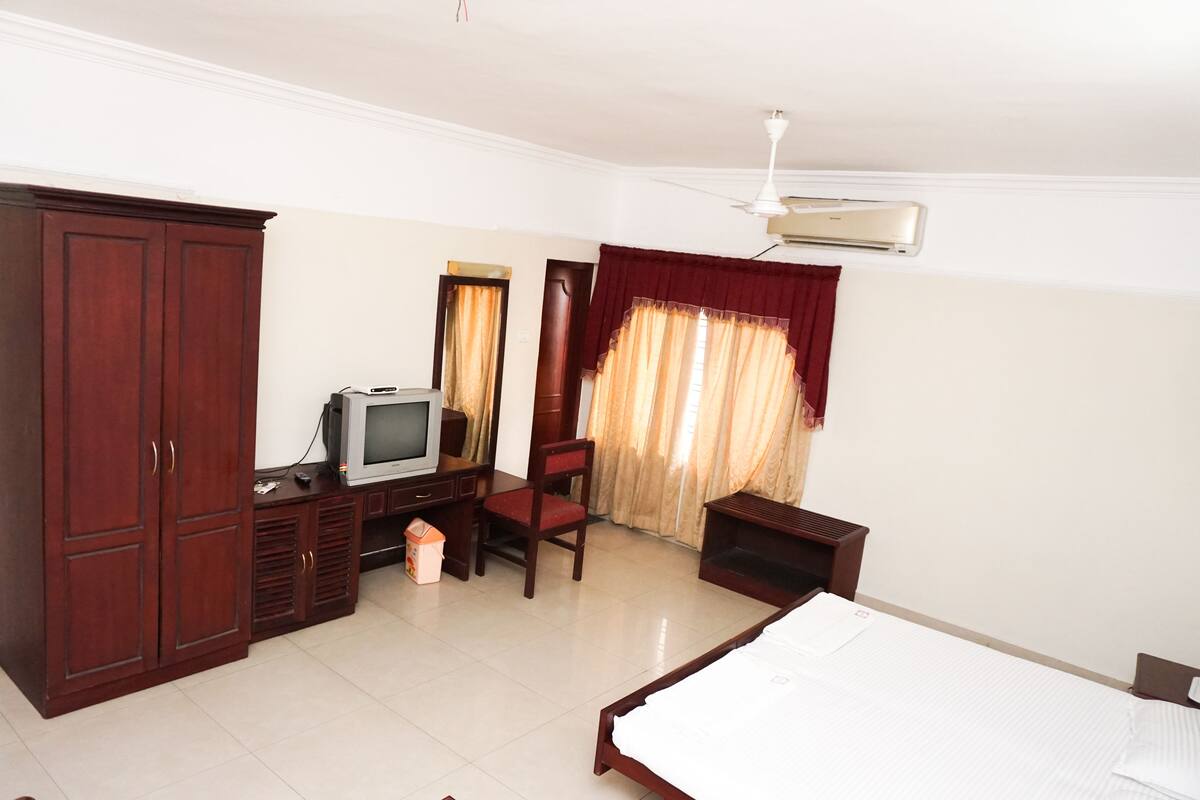 A hotel room with a bed, wardrobe, desk, chair, television, and curtains.