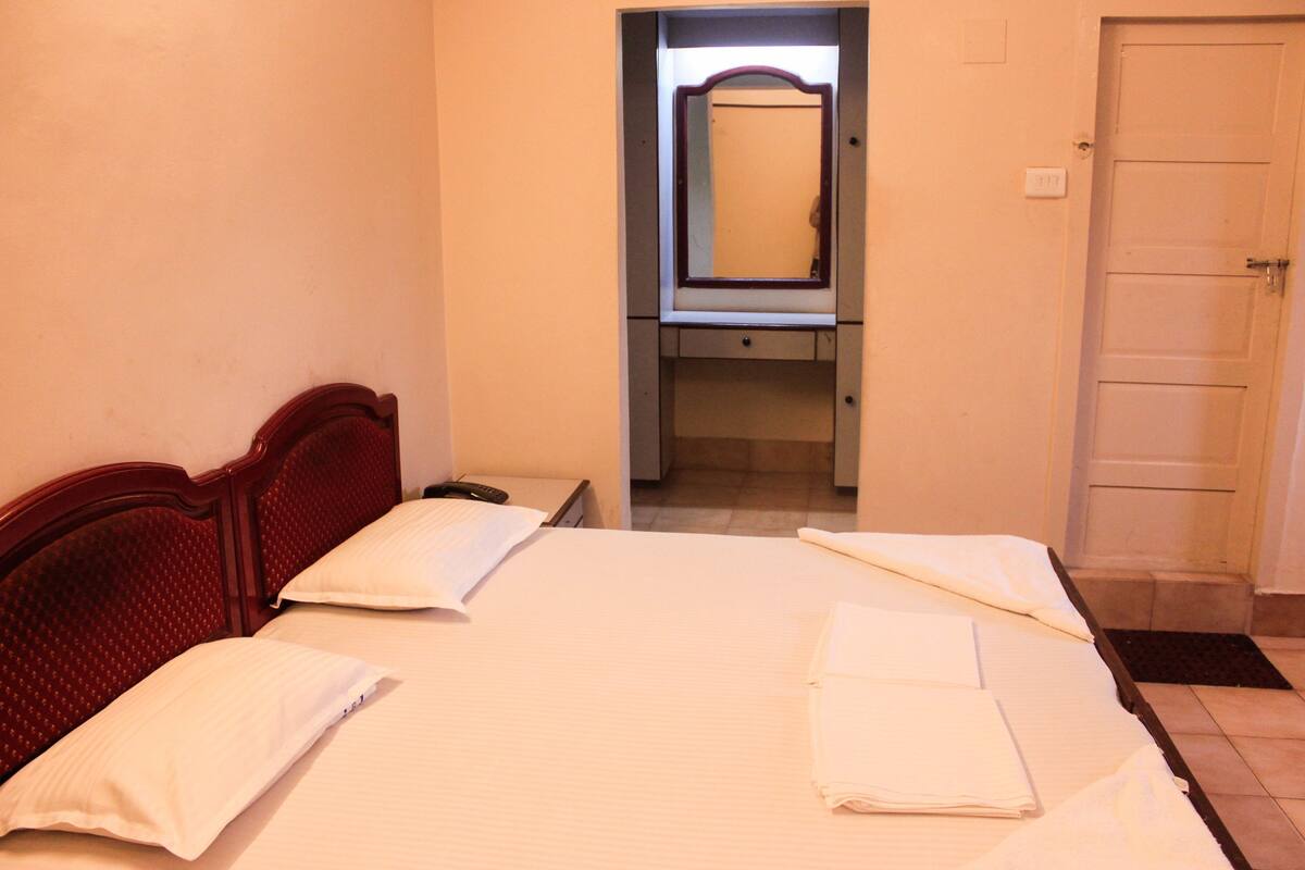 A hotel room with a bed, a mirror, a bedside table, and a door.