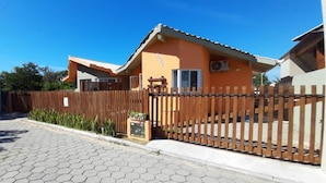 A two-story house with a tiled roof, a wooden fence, and a paved driveway. - Bangalô Red Moon (Florianópolis)