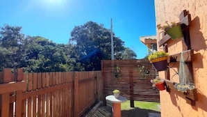 A wooden fence, a small round table, and potted plants on a balcony. - Bangalô Red Moon (Florianópolis)