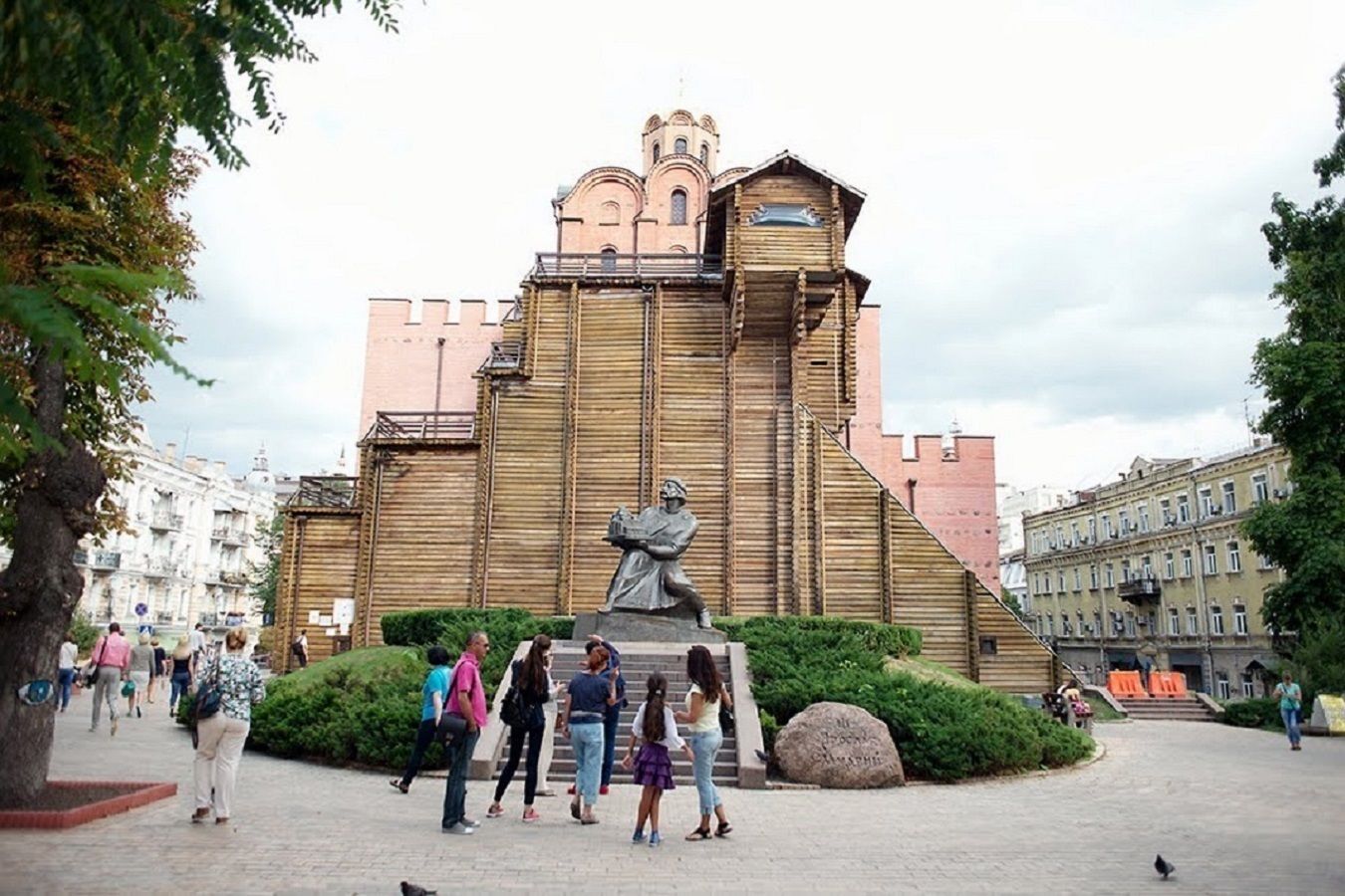 A large building with a statue in front, surrounded by people and greenery.