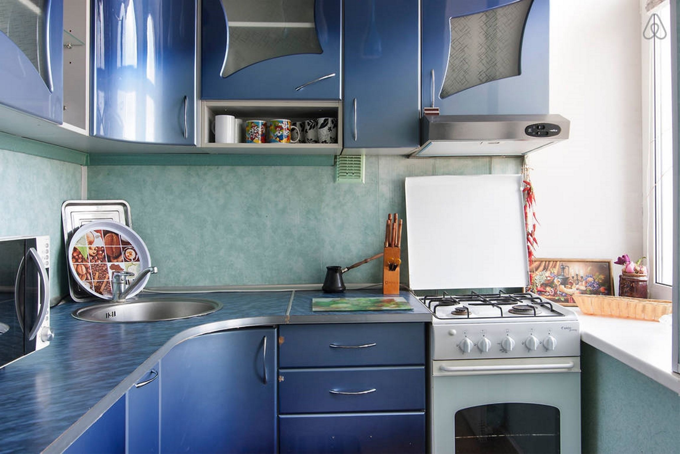 A kitchen with blue cabinets, a stove, a sink, and a microwave.