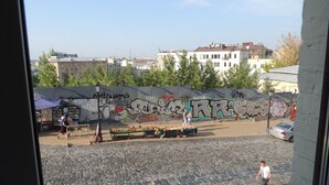 A courtyard with cobblestone pavement, graffiti on a wall, and a few people walking. - Podol Apartment (Kyiv)
