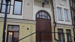 A building with a large wooden door, a small window with iron bars, and a street lamp. - Podol Apartment (Kyiv)