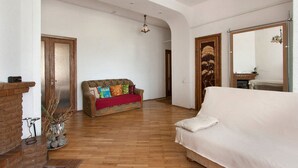 A spacious living area with a wooden floor, a sofa with colorful cushions, a white sofa, and a fireplace. - Podol Apartment (Kyiv)