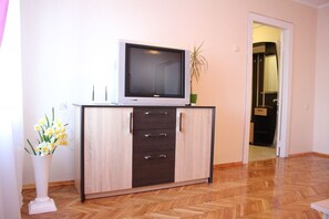 A room with a wooden herringbone floor, a white cabinet with a flat-screen TV on top, and a vase with flowers. - Podol Apartment (Kyiv)