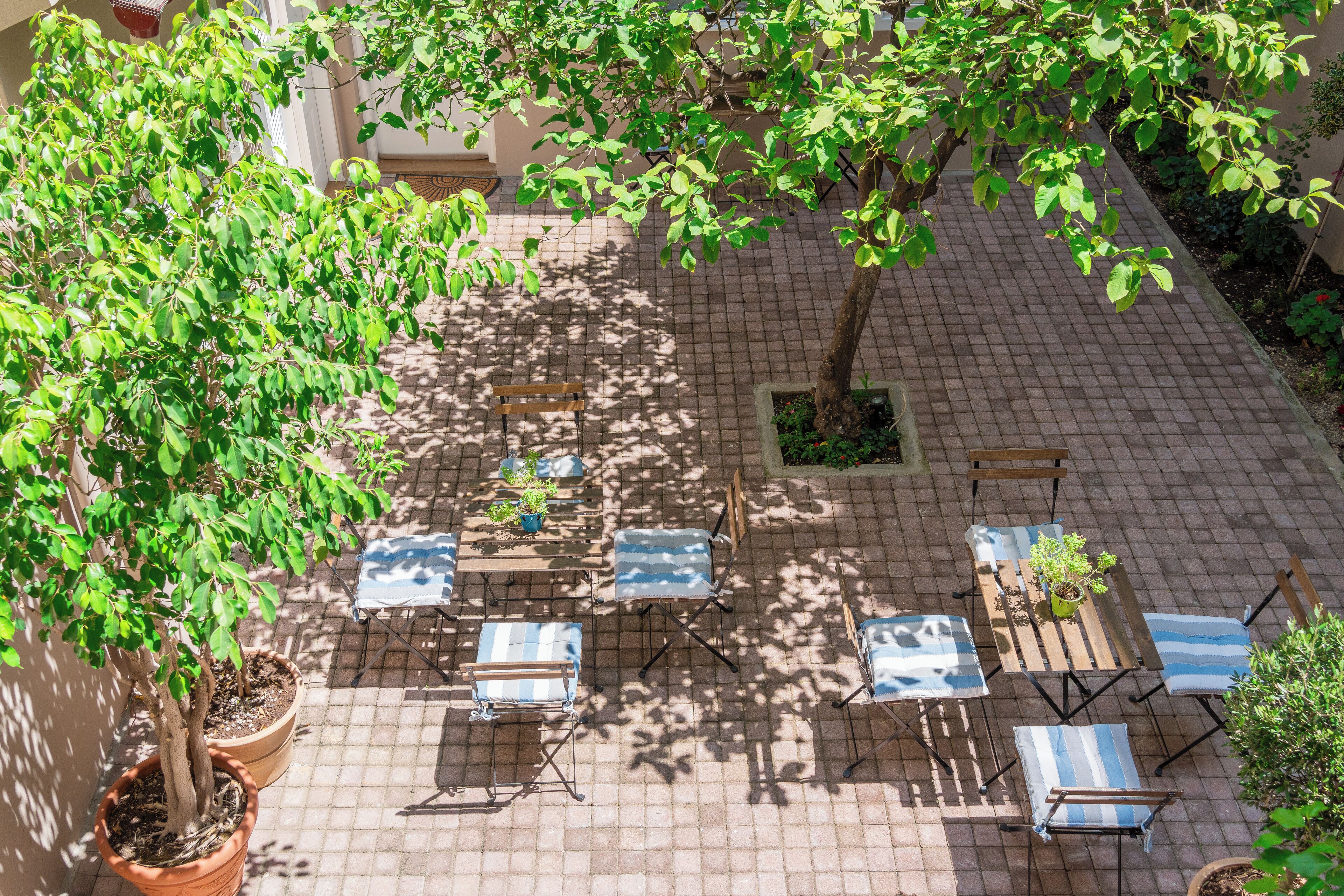 Une terrasse extérieure avec un sol en briques, plusieurs tables et chaises, et des plantes en pot.