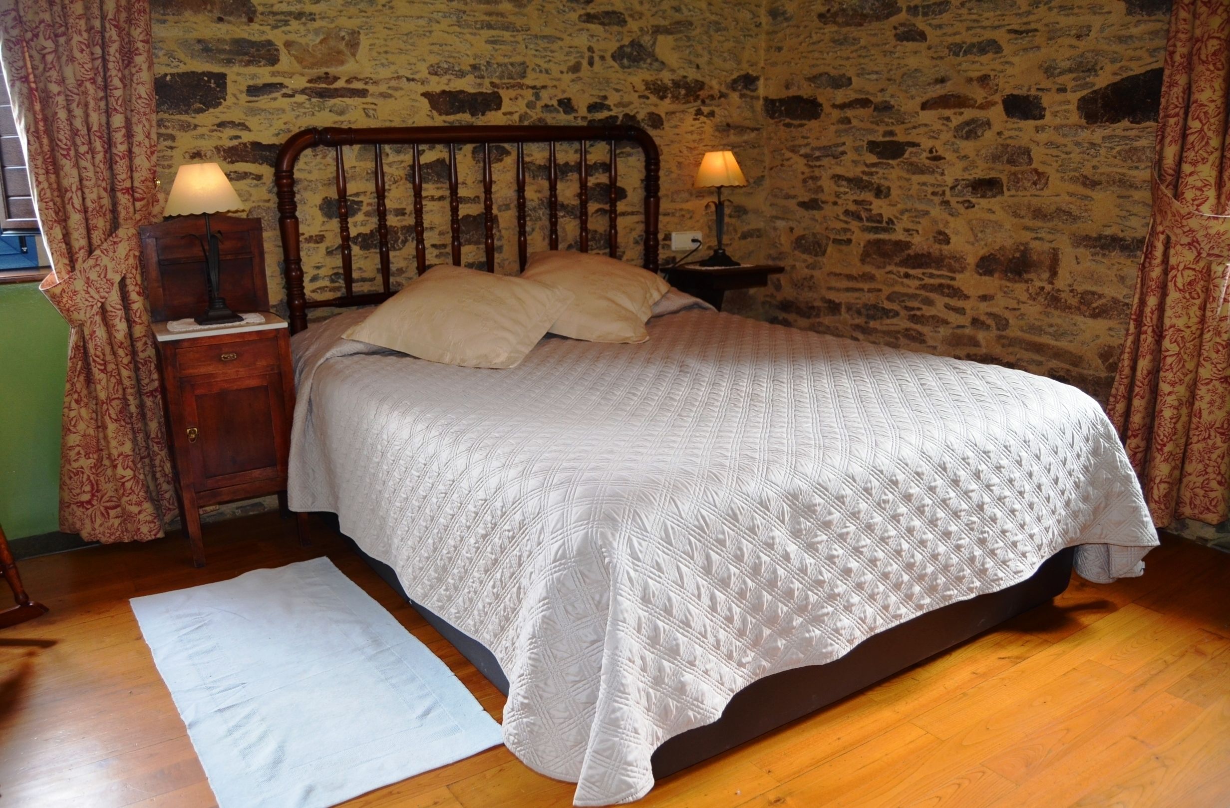 Una cama con cubrecolcha blanco acolchado, cabecera de madera y dos lámparas de noche.