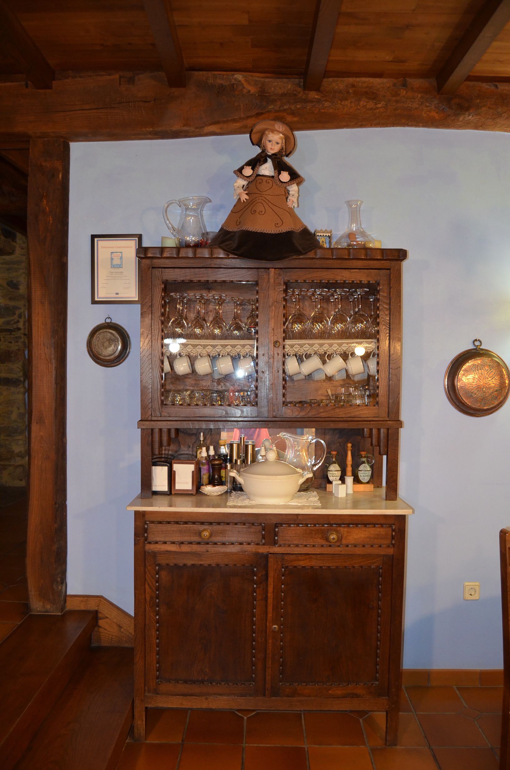 A wooden cabinet with glassware and bottles, a framed certificate, and a copper pot on the wall.