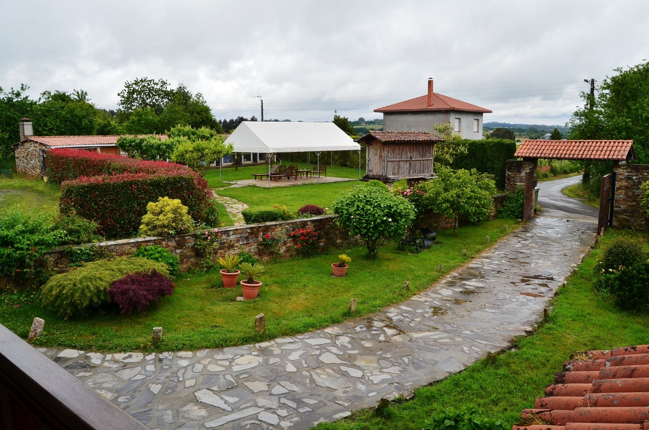 A stone pathway leading to a rustic house with a white canopy and a red-tiled roof.