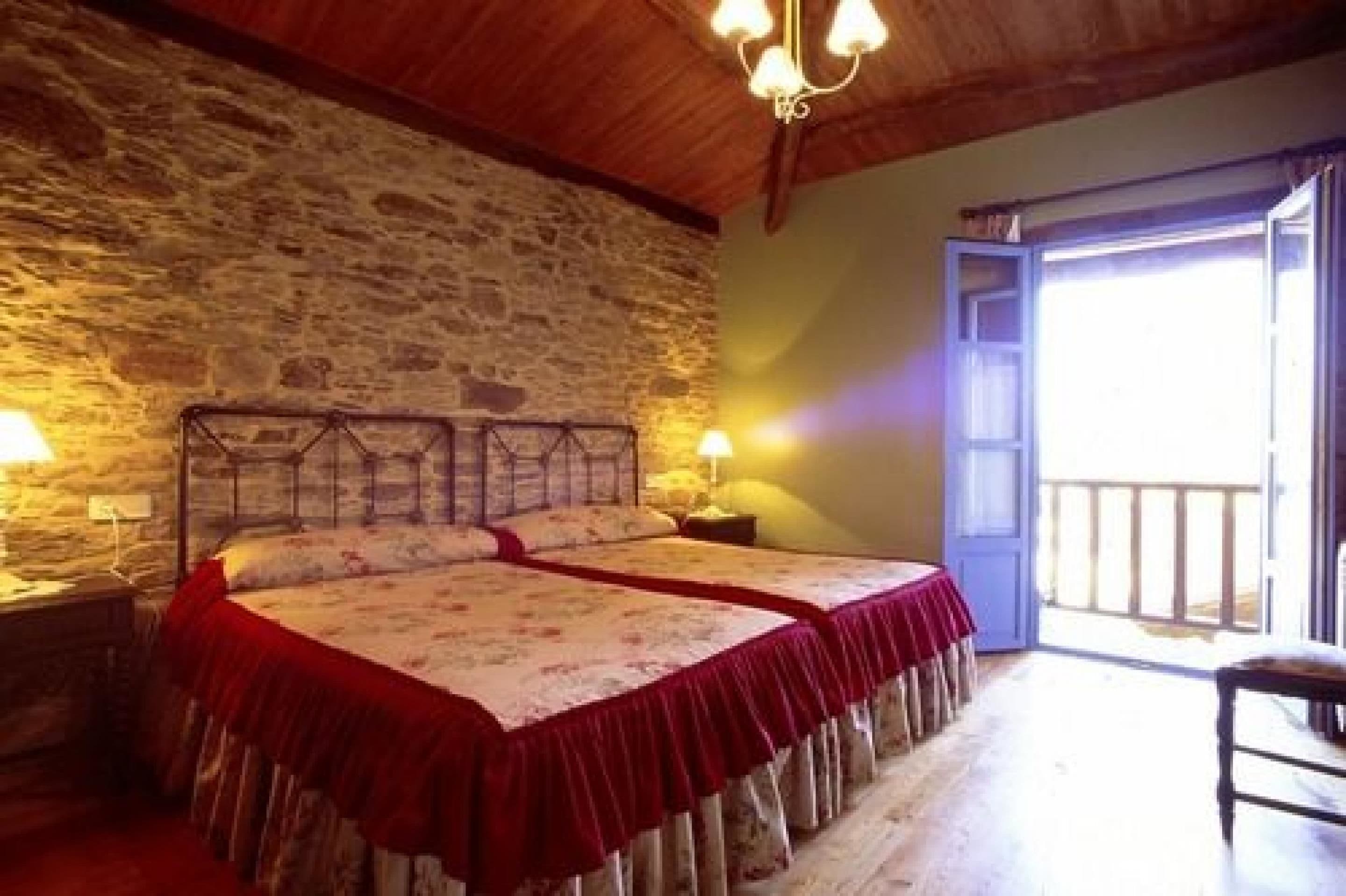 A room with two beds, a stone wall, a wooden ceiling, and a balcony with a railing.