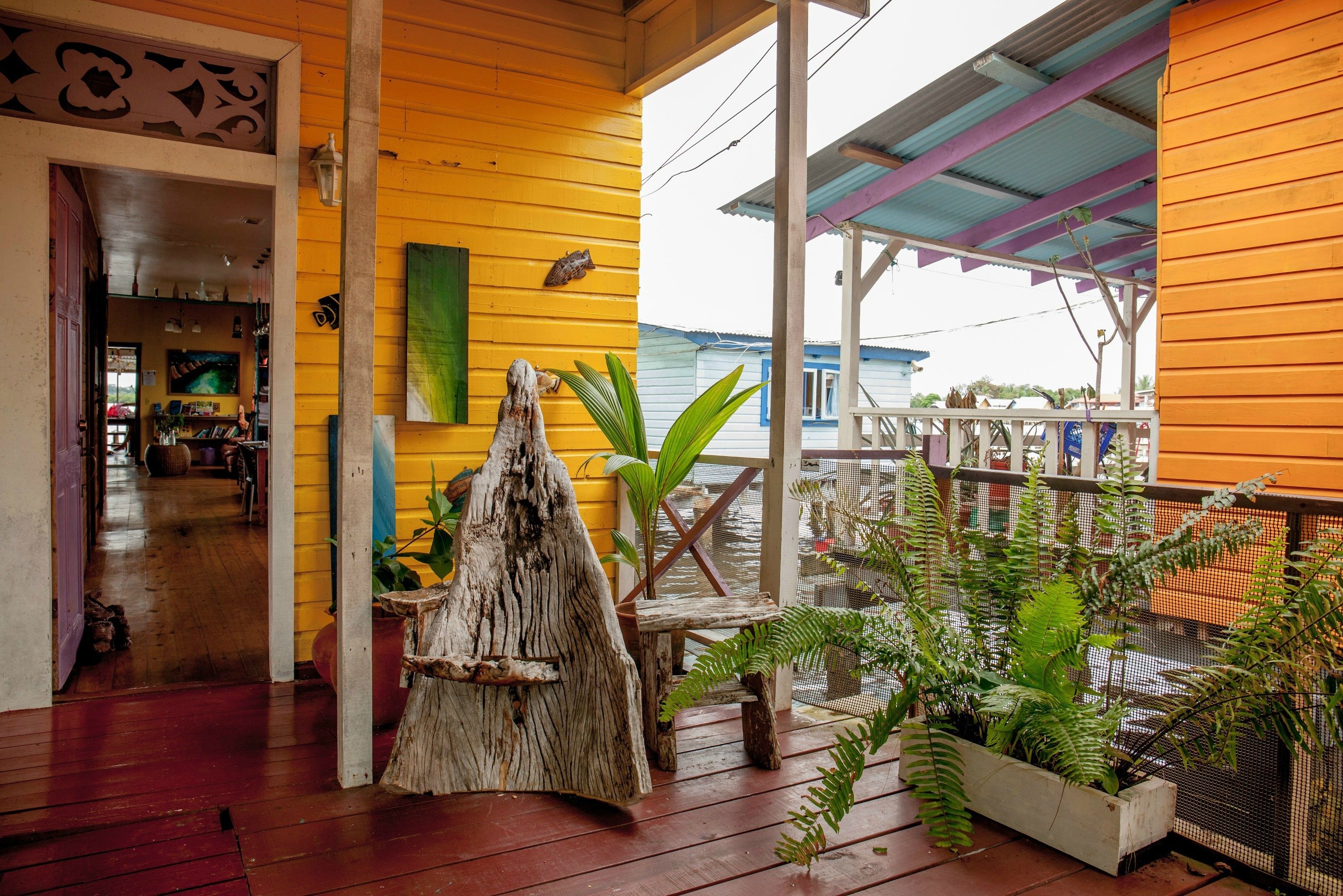 A wooden porch with a rustic design, featuring a wooden bench, a decorative tree stump, and various potted plants.