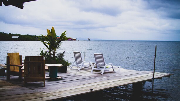 A wooden dock with two lounge chairs and a table, overlooking a calm body of water with distant land and a cloudy sky. - Barrbra BnB Over The Sea (Bocas del Toro)