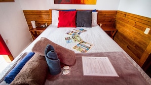 A neatly made bed with a patterned bedspread, two pillows, a set of cards, a rolled towel, and a piece of paper on the bed. - Barrbra BnB Over The Sea (Bocas del Toro)