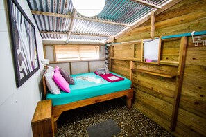 A small, rustic room with a wooden bed, a small window, and a wall-mounted mirror. - Barrbra BnB Over The Sea (Bocas del Toro)