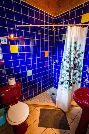 A bathroom with blue tiled walls, a red toilet, a white sink, and a shower curtain with a tree pattern. - Barrbra BnB Over The Sea (Bocas del Toro)