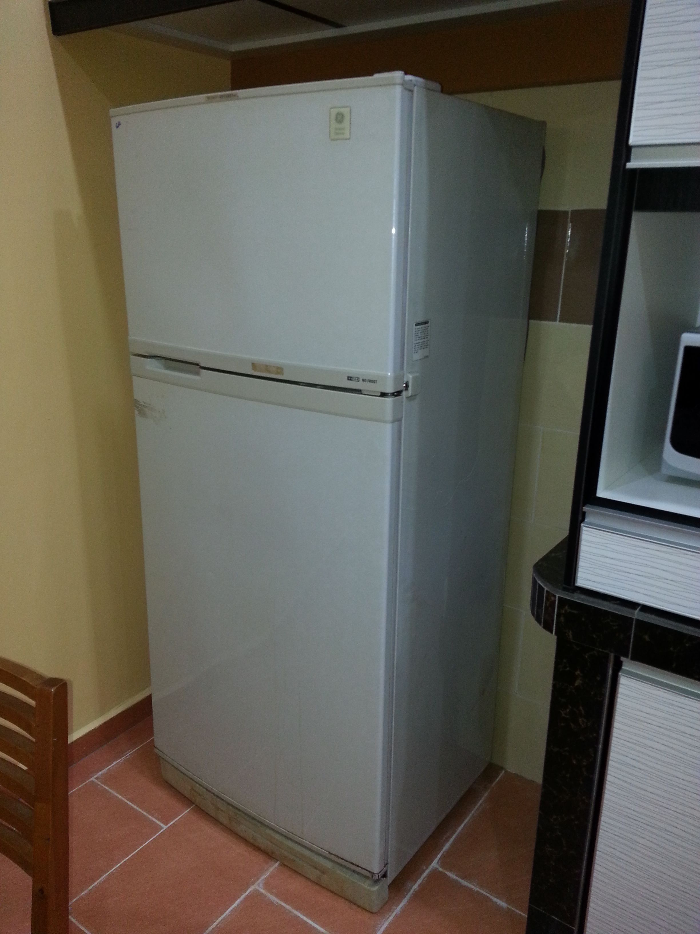 A compact white refrigerator in a kitchen with tiled walls and a wooden chair.