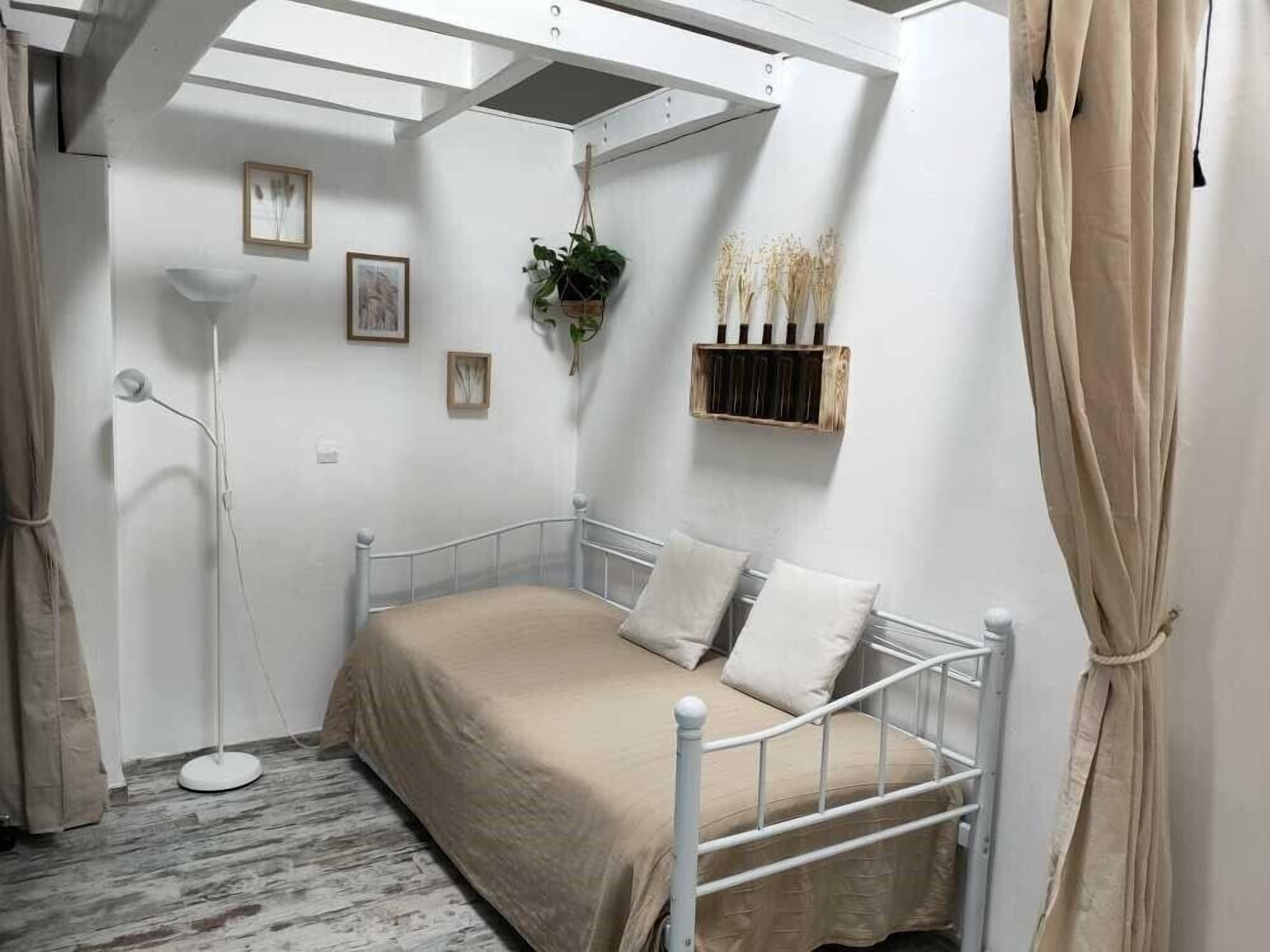 A bedroom with a metal bed frame, a beige bedspread, and a white floor lamp.